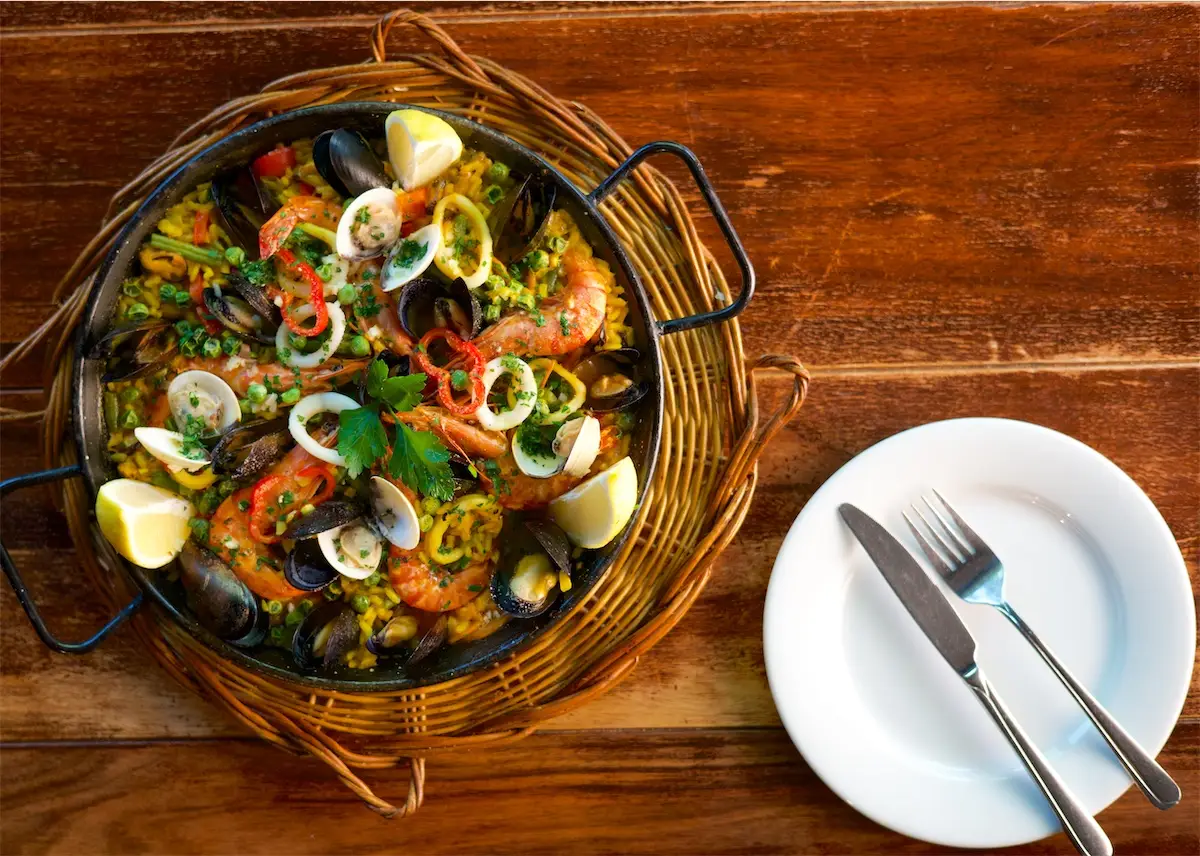 Paella in der Pfanne, daneben ein gedeckter Teller